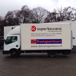 hier zie je een vrachtwagen waar reclame op staat en het logo van het bedrijf de transporteurs